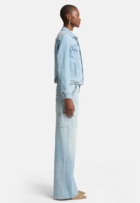 Ljusblå denimjacka med fickor och knappar, ihop med vida ljusblå jeans med sidofickor. Slät textur.