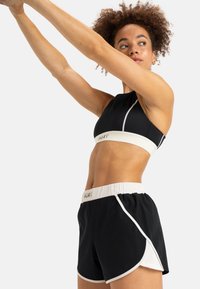 Zwarte sportbeha met witte accenten en logo, gecombineerd met zwarte shorts met witte rand en elastieken tailleband, geschikt voor actieve kleding.