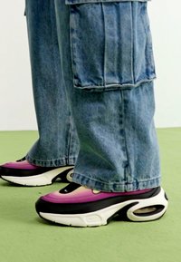Black and pink sneakers with a smooth leather upper, thick white sole, and air cushioning. Worn with baggy blue denim pants.