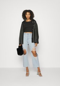 Top cropped preto, casaco de pele preto oversized, jeans de perna larga rasgados azul claro com bainhas desfiadas, bolsa de pelúcia preta, sandálias de salto com padrão.