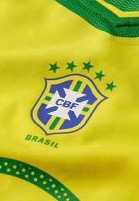 Brazil national football team jersey in vibrant yellow, featuring green accents, a shield-shaped logo with stars, and "BRASIL" text.
