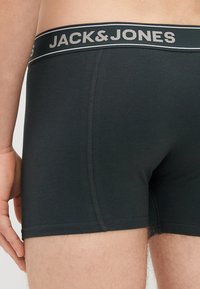 Črne boksarske hlače z širokim pasom, na katerem je v sivi barvi napisan "JACK&JONES". Tkanina je gladka, s ravnimi šivi za udobje.