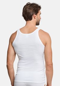 Hvid bomulds tanktop med en tætsiddende design, brede skulderstropper og en ribbet tekstur, båret af en mand set fra ryggen.