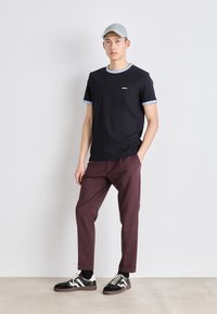 Svart t-skjorte med lyseblå ribbing, logo på brystet, kombinert med burgunder bukser som smalner inn mot ankelen og svarte sneakers med hvite accenter. Lys caps på hodet.