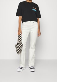 Camiseta de algodón negra con diseño gráfico, vaqueros de mezclilla blancos, bolsa a cuadros en blanco y negro, y zapatillas negras con suelas blancas.