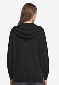Czarny kaptur z luznym krojem, ściągaczami przy rękawach oraz u dołu. Wykonany z miękkiego materiału, charakteryzujący się prostym wzornictwem bez widocznych wzorów.