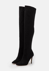 Botas negras hasta la rodilla, hechas de ante suave, con punta afilada y tacón de aguja, con un diseño ajustado que abraza la pierna.