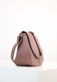 Różowa skórzana torebka o strukturalnym kształcie, z plecionym uchwytem i złotym metalowym elementem. Gładka tekstura i minimalistyczny design.