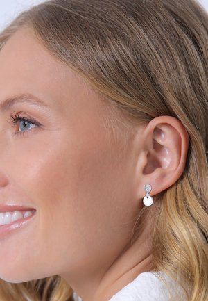 Orecchini in argento con un perno circolare e un pendente rotondo bianco. Presentano un dettaglio scintillante sul perno, enfatizzando un design elegante.