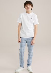 Vit kortärmad t-shirt med en liten svart logotyp, tillsammans med ljusblå rutiga byxor och vita sneakers med blå detaljer.