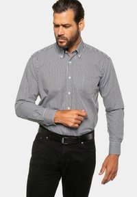 Herre skjorte med knapper lavet af sort og hvidt gingham ternet stof, lange ærmer, button-down krave, parret med et sort bælte og mørke jeans.