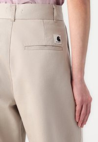 Pantaloni beige in cotone, con una tasca posteriore dotata di un'etichetta quadrata, linee pulite e una vestibilità su misura in vita.