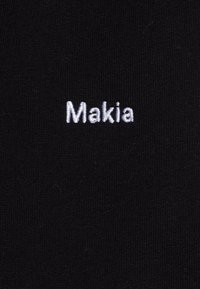 Tessuto nero con il testo ricamato "Makia" in filo bianco. Il tessuto ha una superficie liscia e un motivo a maglia costante.