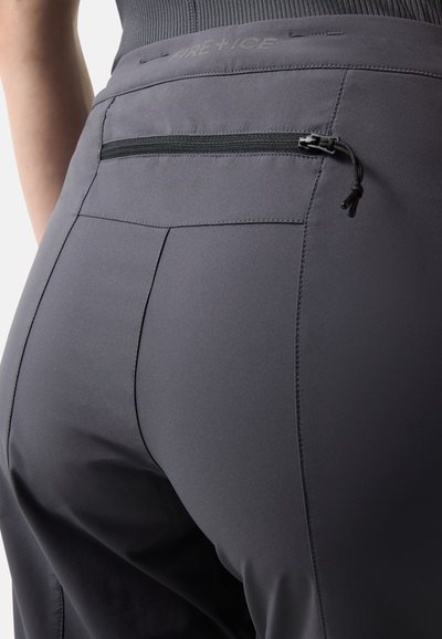 Detailní záběr zadní části šedých kalhot s černým zipovým kapsou a jemným nápisem "FIRE+ICE" na pasu.