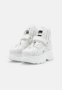 Adidași înalți albi, cu un superior din piele sintetică netedă, guler căptușit, curea ajustabilă și talpă din cauciuc albă masivă.