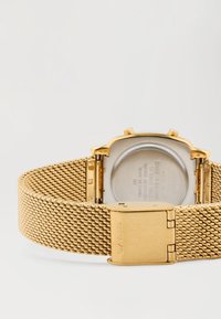 Pulseira de metal em malha dourada com fecho aberto, mostrando a parte de trás do estojo em aço inoxidável com texto gravado e o nome da marca Casio.