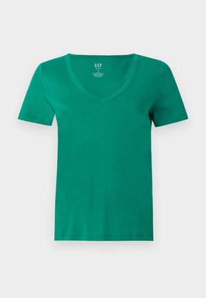 T-shirt vert en coton à manches courtes et col en V, présenté à plat, avec une étiquette de marque GAP visible à l’intérieur du col sur un fond gris clair.