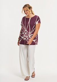 Luftig kortærmet top med stort hvidt blomsterdesign på en mørke lilla baggrund, kombineret med hvide bukser med vide ben.