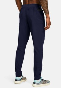 Pantalones deportivos azul marino con cinturilla elástica, bolsillos laterales y un corte ajustado. El material parece suave con un ligero brillo.