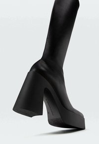 Botte noire à hauteur genoux en cuir lisse, dotée d'un chunky talon haut et d'une semelle plateforme avec un fond texturé pour une meilleure adhérence.