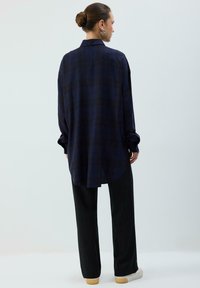 Marineblå ternet skjorte med knapper, lange ærmer, afslappet pasform, buet kant, kombineret med sorte bukser med vide ben og hvide sneakers.