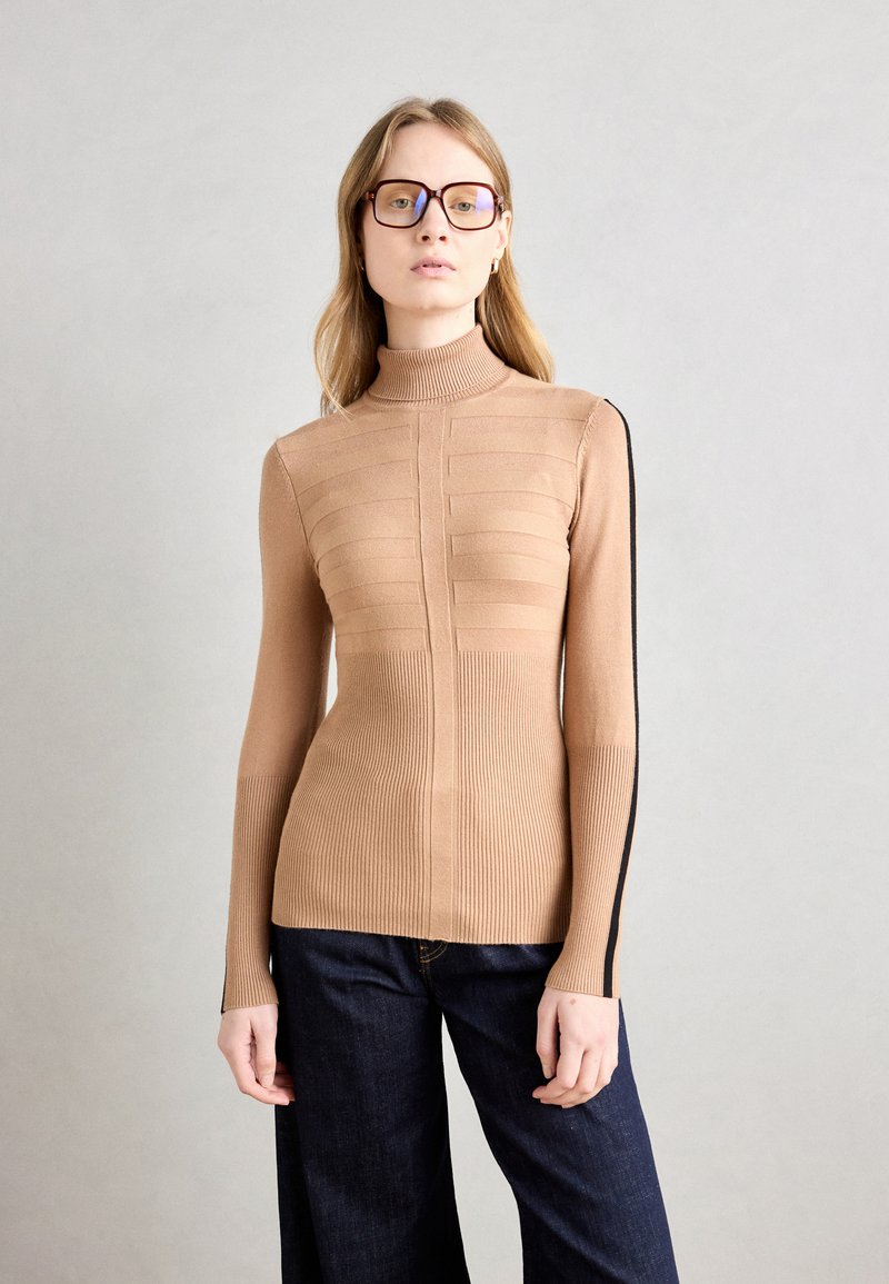 Strakke coltrui in een gedempt beige, met ribbelstructuur, horizontale lijnen over de borst en zwarte accenten aan de zijkanten.