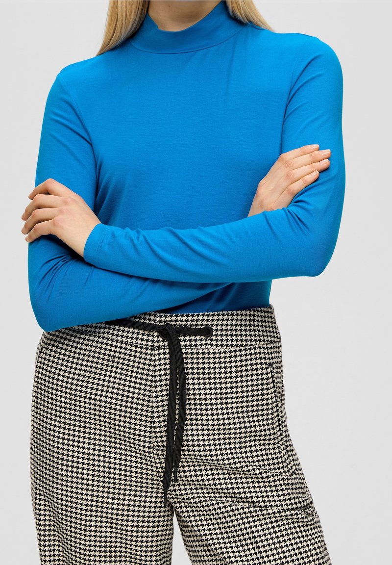 Langdurige mouw, coltrui in felblauwe stof, gecombineerd met een broek met een houndstooth-patroon, voorzien van een zwarte trekkoord.