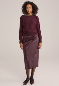 Burgundský svetr s kulatým výstřihem, doplněný elegantními, splývavými koženými sukněmi ke kolenům v ladící barvě. Celkový vzhled završují jehly s špičatou špičkou.