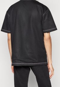 Svart mesh t-shirt med kort ärm och lös passform, med en rund halsringning och kontrasterande vit sömnad längs kanterna.