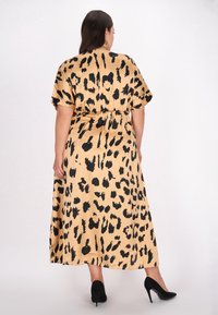 Maxikjole i silkeagtigt beige stof med sort leopardprint, korte ærmer og elastisk talje. Sorte højhælede sko fuldender looket.