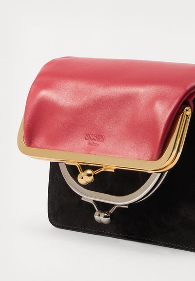 Sort suede taske med en glansfuld pink klap, guld- og sølvhardware, der har en cirkulær ramme og en låse-detalje.