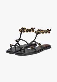 Sandali flat neri con design a infradito, dotati di una fibbia decorativa in oro e pietra nera sul cinturino alla caviglia. Materiale in pelle liscia.