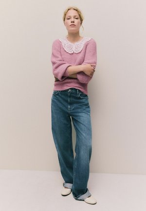 Rosa Strickpullover mit einem weißen Spitzenkragen, kombiniert mit lockeren blauen Denim-Jeans und cremefarbenen Schuhen. Texturiertes Material und lockere Passform.