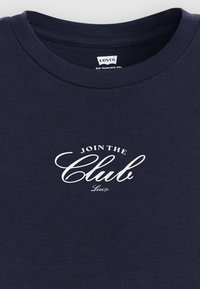 T-shirt de algodão azul-marinho com gola redonda e um logótipo branco impresso "JOIN THE Club". O texto tem uma fonte cursiva, adicionando detalhe.