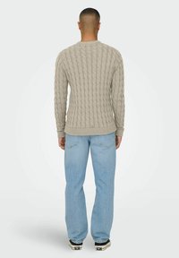 Pull en maille grise à côtes, porté sur un jean bleu clair, avec vue de dos et une finition lisse.