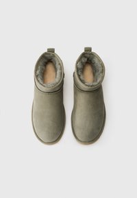 Par de botas de ante gris hasta el tobillo con forro de piel sintética y suelas de goma, mostradas desde arriba sobre un fondo blanco.