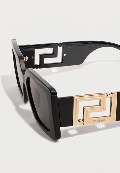Μαύρα ορθογώνια γυαλιά ηλίου με παχιά πλαϊνά και χρυσά γεωμετρικά διακοσμητικά λογότυπα Versace στις πλευρές.