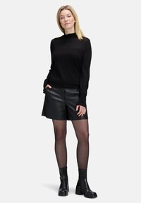 Zwarte gebreide trui met een hoge hals en ruches, gecombineerd met zwarte nepleer shorts en zwarte enkellaarsjes met een chunky hak.