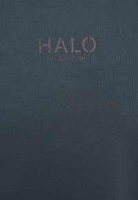 Mørk teal bomuldsstof med en ribbet struktur, prydet med ordet "HALO" i lys brun og et numerisk design nedenunder.