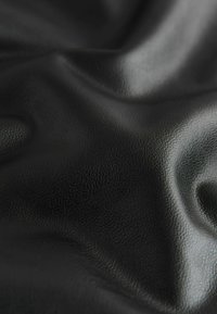 Czarna skóra z fakturowaną, lekko kamienistą powierzchnią, delikatnie zwisająca, aby pokazać swoją elastyczność i głębokość koloru.