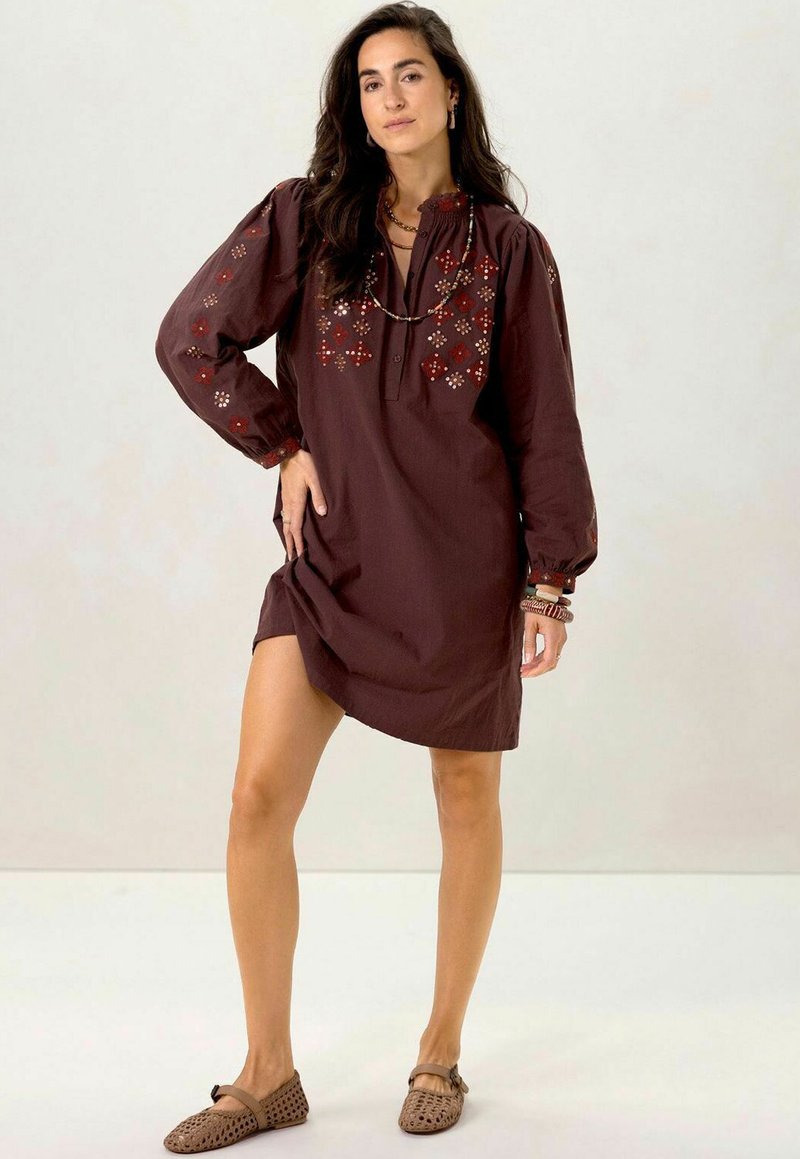 Robe en coton brun avec de longues manches bouffantes, motifs floraux brodés en rouge et beige, et une patte de boutonnage au niveau du col.