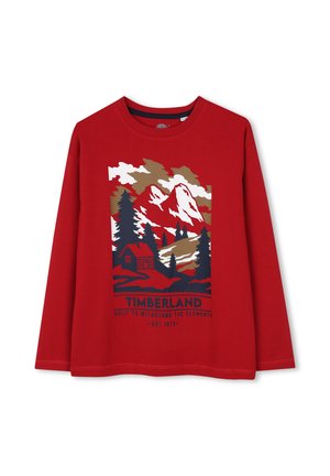 Rood shirt met lange mouwen met een berg-, bomen- en huttenafbeelding en de tekst "Timberland Built to Withstand the Elements Est. 1973" aan de voorkant.