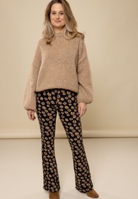 Beige gebreid trui met verlaagde schouders, gecombineerd met zwarte flared broeken met een bloemenpatroon in roze en geel. Bruine enkellaarsjes.