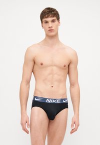 Des slips de sport noirs avec une large ceinture navy à motifs mettant en valeur le logo Nike de manière proéminente. Design lisse et ajusté.