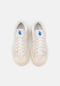 Paire de baskets New Balance blanc cassé avec détails en mesh et en suède, lacets blancs et logos New Balance bleus sur les languettes, vues de dessus.