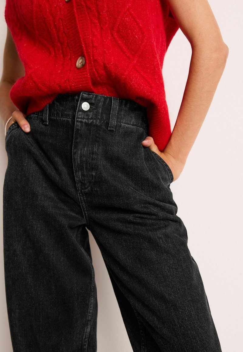 Zwarte denim high-waisted jeans met zakken en een zilveren knoopsluiting, gecombineerd met een rode gebreide trui met een kabelpatroon.