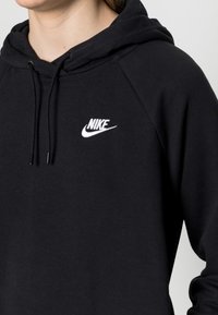 Sudadera negra de tela suave, con un logo blanco de Nike en el pecho, cordones en la capucha y puños acanalados.