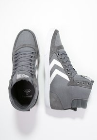 Sapatilhas altas cinzas com detalhes brancos, apresentando uma combinação de materiais de tecido e camurça, ponta redonda e colarinho almofadado para conforto.