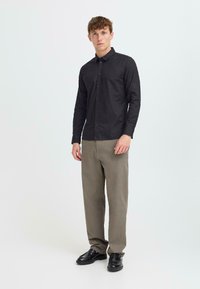 Long-sleeve black button-up shirt, textured fabric, paired with light brown straight-leg pants and black shoes. Simple design, no patterns.