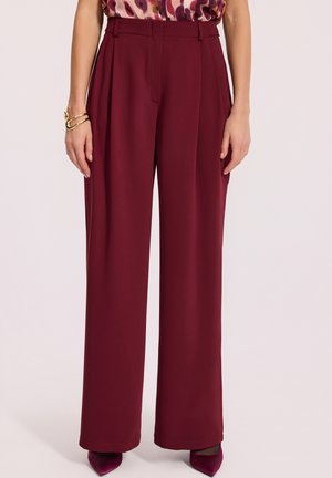 Spodnie o szerokich nogawkach wykonane z bordowego materiału, z plisami i dopasowanym paskiem. W połączeniu z czółenkami w bordowym kolorze.